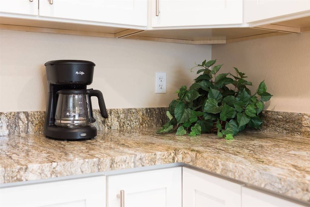 A kitchen with a coffee maker on the counter and a potted plant beside it.