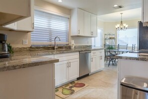 A modern kitchen with white cabinets, a granite countertop, a dishwasher, and a dining area with a table and chairs.