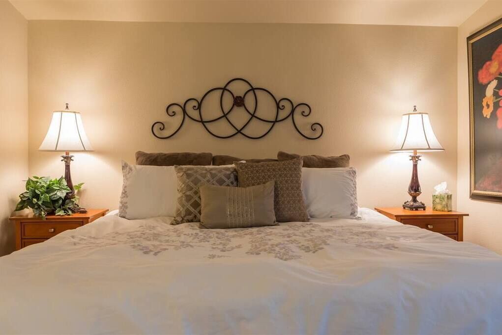 A neatly made bed with a decorative headboard, two bedside tables with lamps, and a framed picture on the wall.
