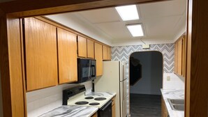 Une cuisine compacte avec des meubles en bois, un micro-ondes noir, un réfrigérateur blanc, une cuisinière et un crédence décorée.