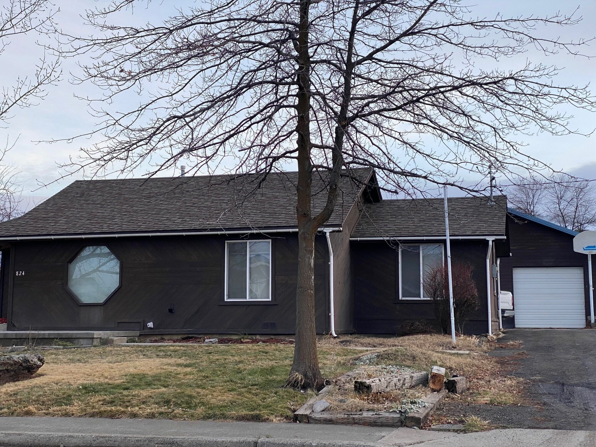 A two-story house with a dark exterior, a garage, and a tree in front.