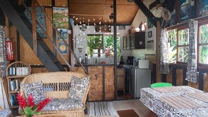 A rustic cabin with a dining area, kitchen, and a staircase leading to a loft. - Fare Vahine Oviri (Avera)