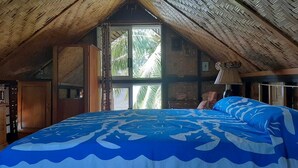 A bedroom with a large bed, wooden ceiling beams, and a window with a view of palm trees. - Fare Vahine Oviri (Avera)