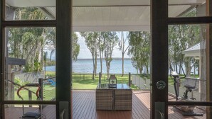 A view from a room with a wooden deck overlooking a lake, featuring exercise equipment and a grill. - Getaway Lakefront environmental House with Kayaks Water Views (Chain Valley Bay)
