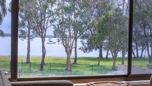 A view from a window overlooking a lake with trees and a boat. - Getaway Lakefront environmental House with Kayaks Water Views (Chain Valley Bay)