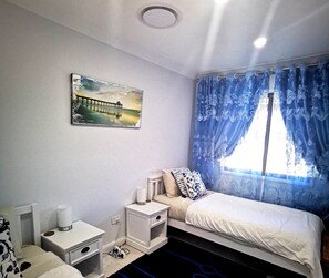Cozy retreat with a neatly made bed, bedside table, and lamp, plus a beautiful painting and window with curtains.