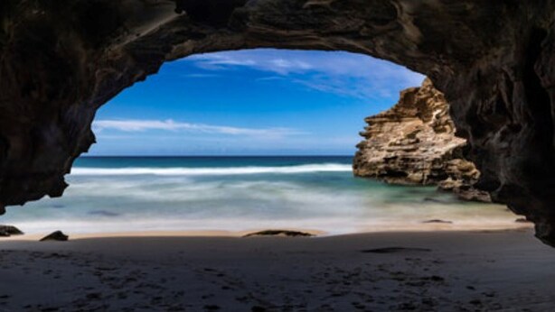 A beach view through a natural rock arch with clear blue water and a sandy shore. - Getaway Lakefront environmental House with Kayaks Water Views (Chain Valley Bay)