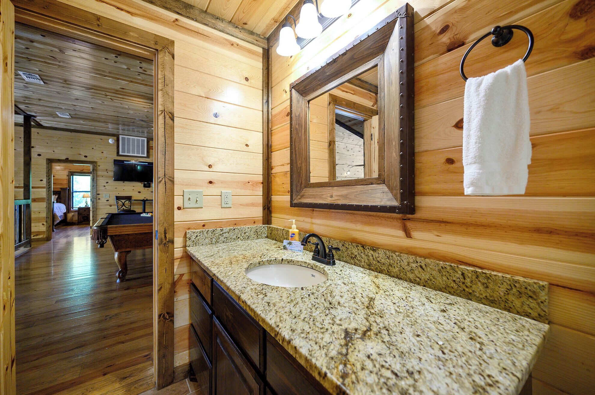 Interior de una cabaña de madera con un lavamanos de encimera de granito, un espejo y una toalla colgada en un aro metálico.