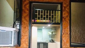 A room with a high ceiling and a woven-patterned wall. There is a bed with an air conditioner, a wooden bench, and a table. - 1-Bed studio apartment in Kabankalan Philippines (Kabankalan, Negros Occidental)
