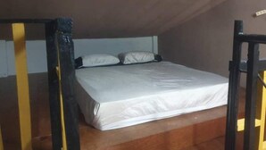 A small, single-bed room with a wooden floor and a sloped ceiling. - 1-Bed studio apartment in Kabankalan Philippines (Kabankalan, Negros Occidental)