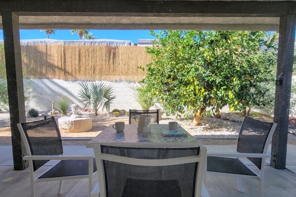 An outdoor patio with a table and chairs, surrounded by a wooden fence and a tree with yellow fruit.