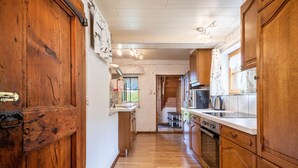 A narrow kitchen with wooden cabinets, a stainless steel refrigerator, and a window with a view.