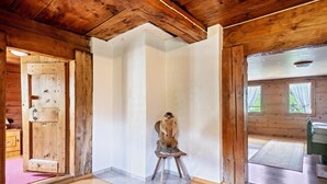 A wooden interior with a wooden door, a small stool, and a view through a window.