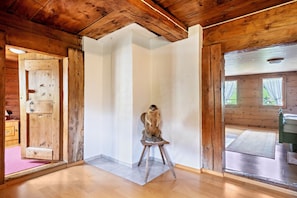 A wooden interior with a wooden door, a small stool, and a view through a window.