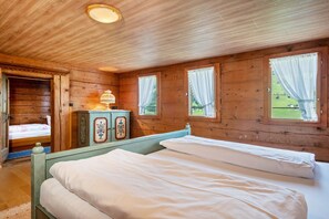 A wooden cabin room with two beds, a dresser, and a window with curtains.