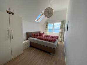 A bedroom with a bed, a wardrobe, a nightstand, a hanging light, a window with a view, and a skylight.