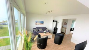 Un salon moderne avec un canapé, une table basse et des chaises noires. Une grande fenêtre offre une vue sur l’extérieur.