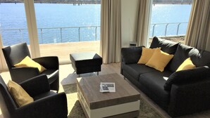 Een woonkamer met uitzicht op een wateroppervlak, een bank, fauteuils en een salontafel.