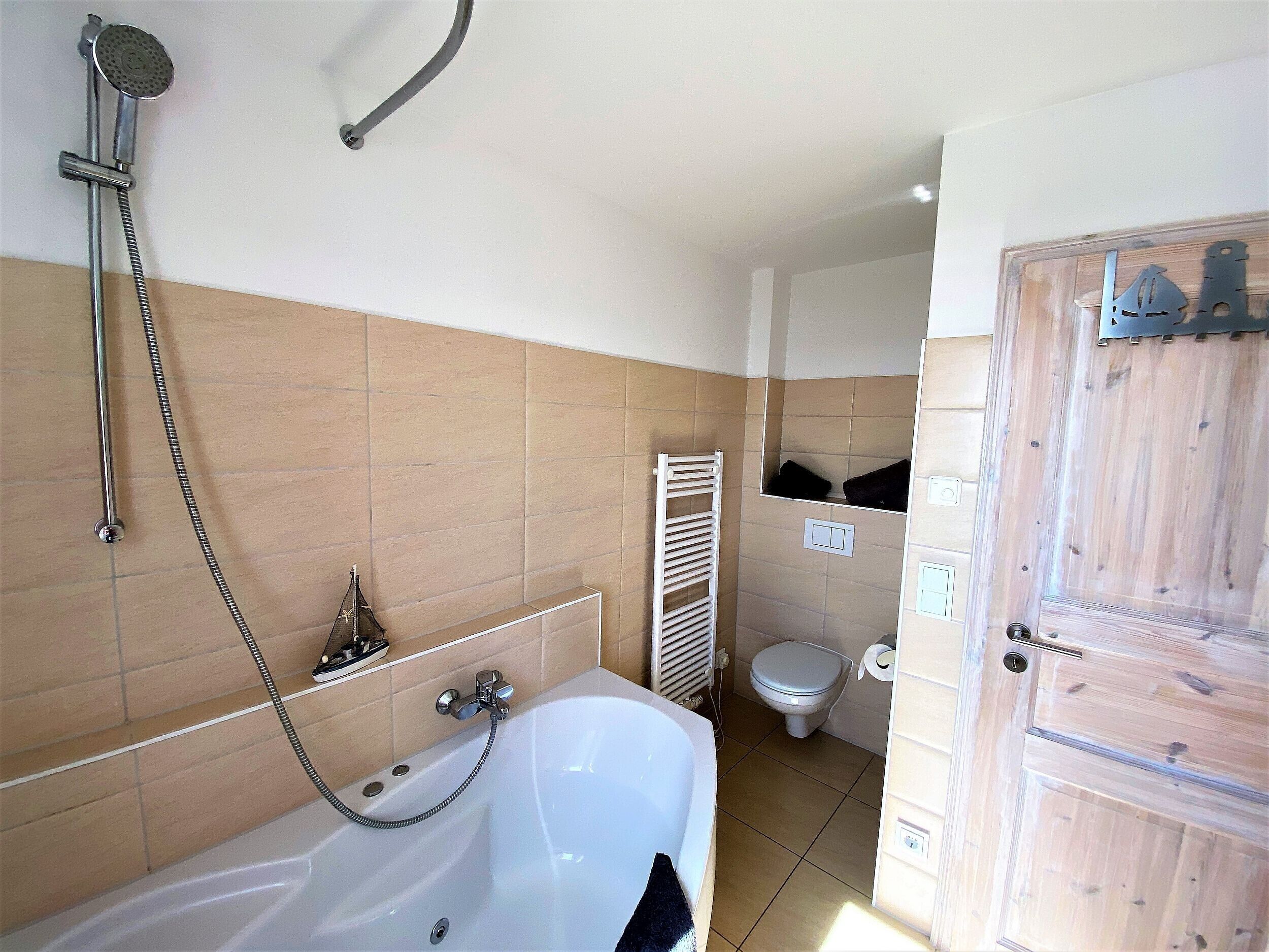 Un baño con bañera, ducha, inodoro y perchero para toallas.