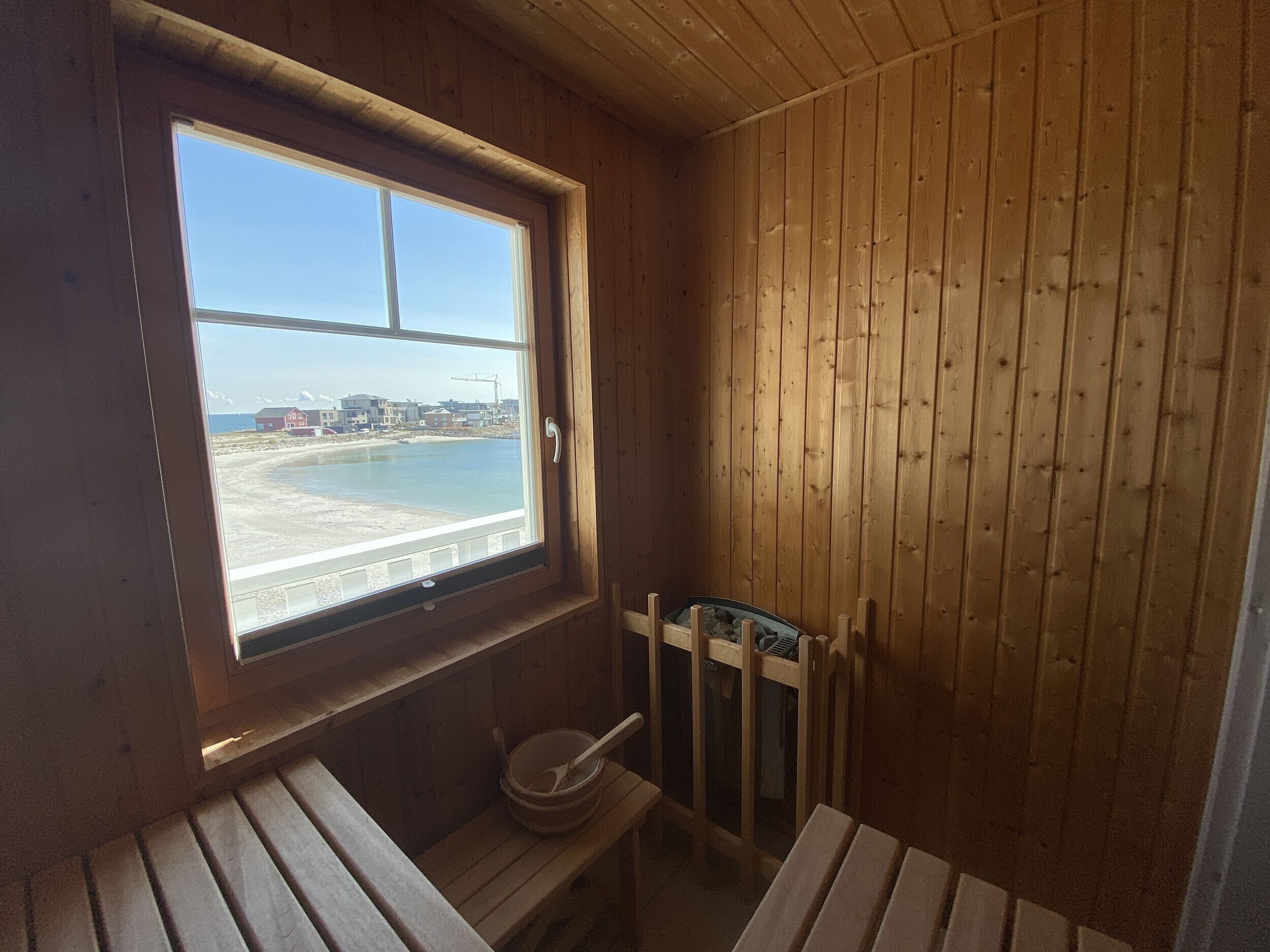A wooden cabin with a window overlooking a beach, a small wooden bench, and a wooden chair.