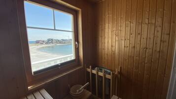 A wooden cabin with a window overlooking a beach, a small wooden bench, and a wooden chair.