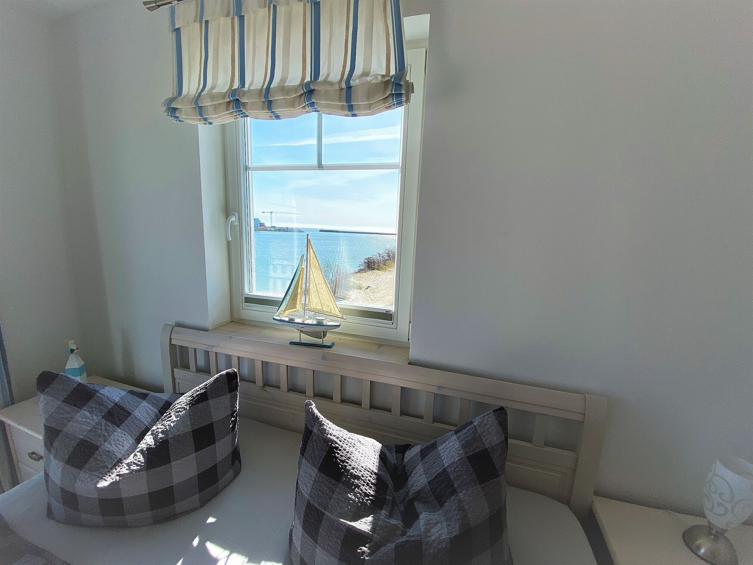 A room with a window overlooking a beach, a small sailboat model, and two checkered bean bag chairs.
