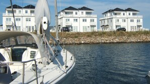 Un voilier est amarré près d’une promenade en bord de mer, avec des immeubles à plusieurs étages en arrière-plan.