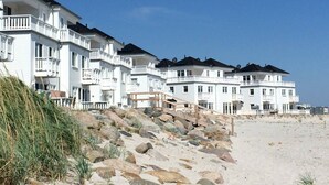 Un hôtel situé en bord de mer, composé de plusieurs bâtiments blancs, doté de balcons et donnant sur une plage de sable.