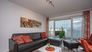 A modern living room with a black leather sofa, a white coffee table, and a view of the sea through large windows. - Vacation Home "Lootsen Hus by Seeblick Ferien" with Sea View (OstseeResort Olpenitz/ Kappeln)
