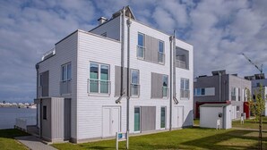 A modern multi-story building with a flat roof, large windows, and a visible outdoor area with a paved walkway. - Vacation Home "Lootsen Hus by Seeblick Ferien" with Sea View (OstseeResort Olpenitz/ Kappeln)