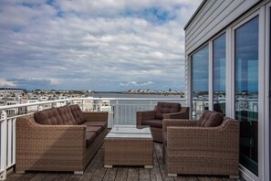 Een balkon met rieten meubels, een glazen tafel en uitzicht op de stad en het water.