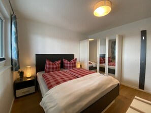 A bedroom with a bed, bedside tables, a nightstand, a mirror, and a wardrobe. - Holiday Apartment "Reeders Nest by Seeblick Ferien" with Sea View (OstseeResort Olpenitz)