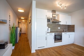 A modern kitchen with white cabinetry, stainless steel appliances, and a wooden floor.