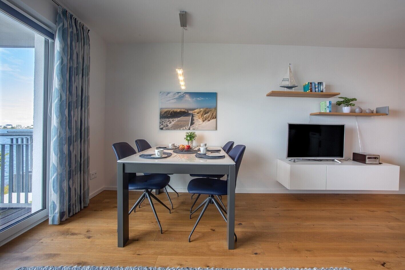A modern living room with a dining area, a flat-screen TV, and a bookshelf.
