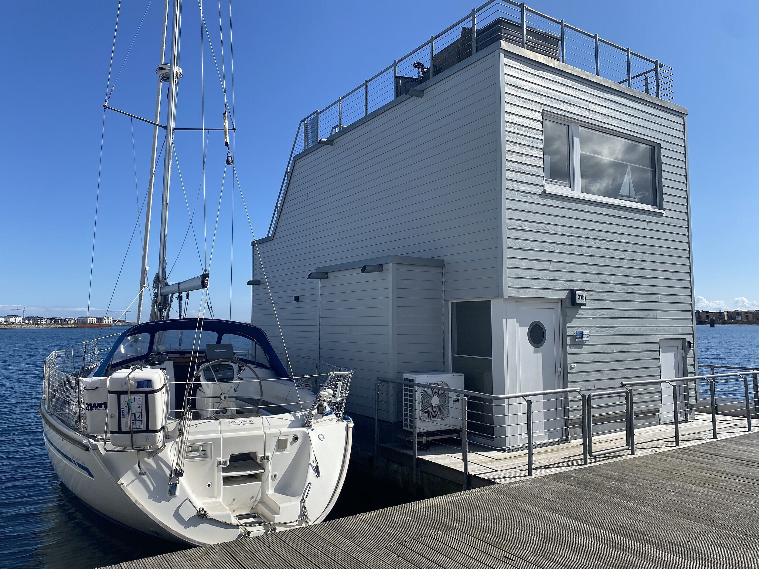 Eine weiße Yacht liegt an einem Steg, in der Nähe befindet sich ein modernes Gebäude.