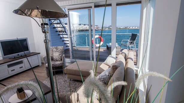 Un salon moderne doté d’un téléviseur, d’un canapé et de grandes fenêtres donnant sur le bord de l’eau.