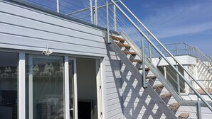 Un escalier menant à un bâtiment doté d’une rampe métallique et d’une porte en verre.