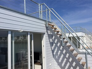 Un escalier menant à un bâtiment doté d’une rampe métallique et d’une porte en verre.