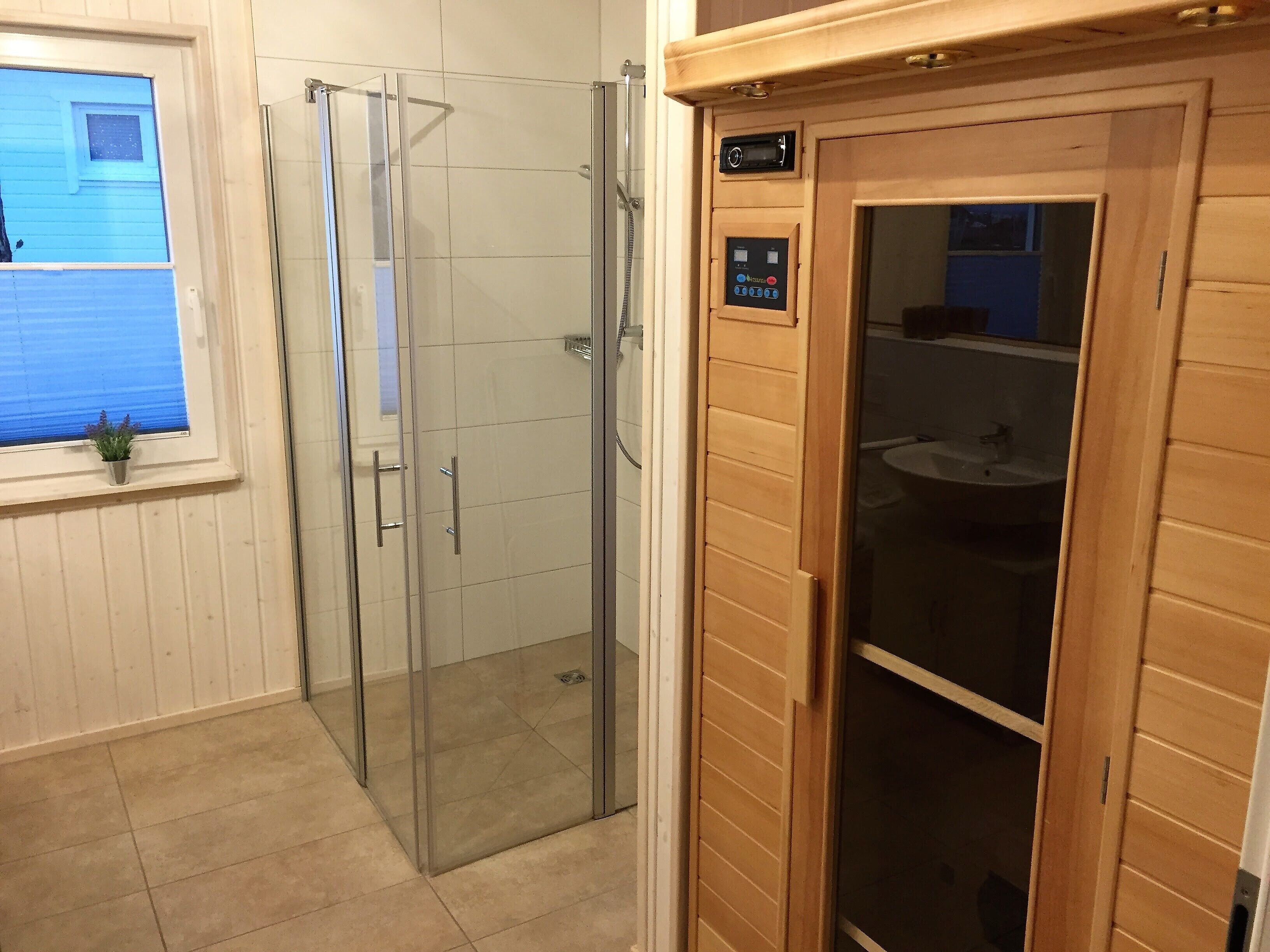 A bathroom with a glass shower enclosure, a wooden vanity, and a window with blinds.