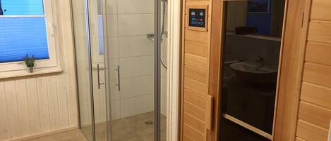 A bathroom with a glass shower enclosure, a wooden vanity, and a window with blinds.