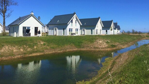 Une rangée de maisons blanches aux toits sombres, une zone herbeuse et une étendue d’eau calme.