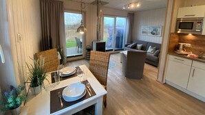 Un intérieur moderne comprenant un coin repas, un canapé, une cuisine et une porte-fenêtre coulissante donnant sur un espace extérieur.