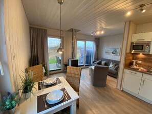 A modern interior with a dining area, a sofa, a kitchen, and a sliding glass door leading to an outdoor area.