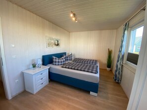 Un dormitorio con cama, mesitas de noche, lámpara de pared y ventana con cortinas.