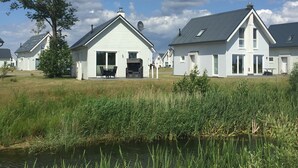 Une rangée de maisons blanches aux toits inclinés, une zone herbeuse et une étendue d’eau au premier plan.