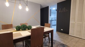 Un comedor con una mesa larga, sillas y un centro de mesa decorativo con plantas. Se ve una cocina al fondo.