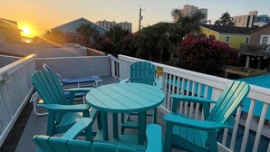 A turquoise deck with a round table and chairs, overlooking a sunset and residential buildings. - Family-Friendly Coastal Retreat with Private Pool | 3BR | Walk to the Beach (South Padre Island)