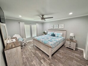 A bedroom with a wooden bed, a ceiling fan, a nightstand, and a chair.