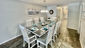 A dining area with a long table, white chairs, and a sign on the wall. - Family-Friendly Coastal Retreat with Private Pool | 3BR | Walk to the Beach (South Padre Island)