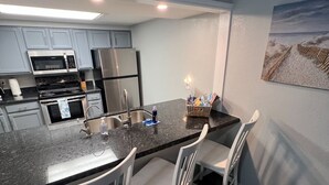 A modern kitchen with granite countertops, stainless steel appliances, and white chairs. - Family-Friendly Coastal Retreat with Private Pool | 3BR | Walk to the Beach (South Padre Island)